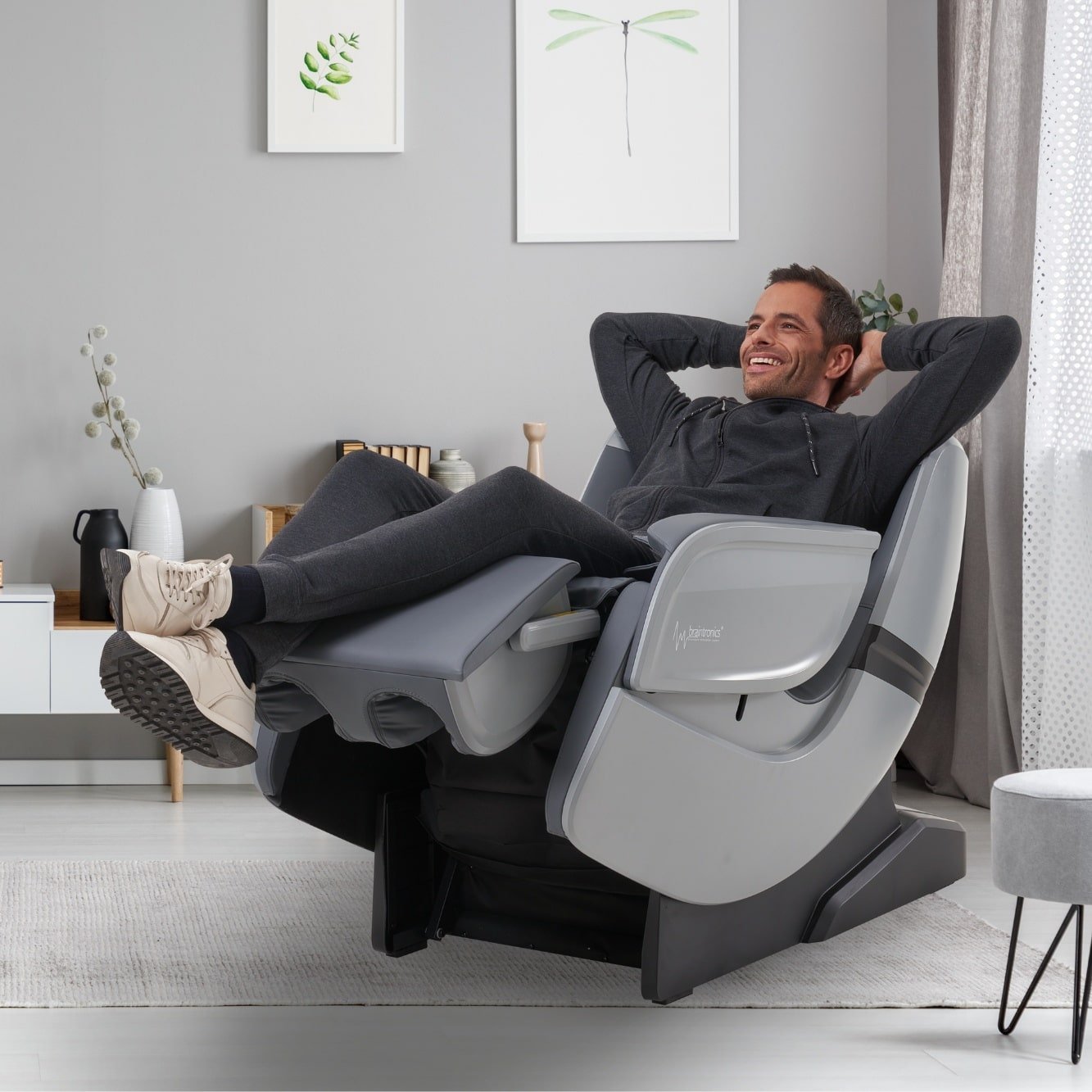 hombre acostado con zapatos en silla de masaje Casada Ecosonic - Plata en la sala de estar