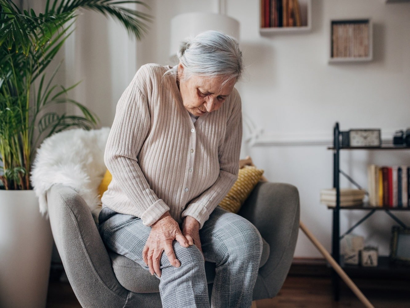 donna anziana in poltrona con dolori muscolari inspiegabili a braccia e gambe